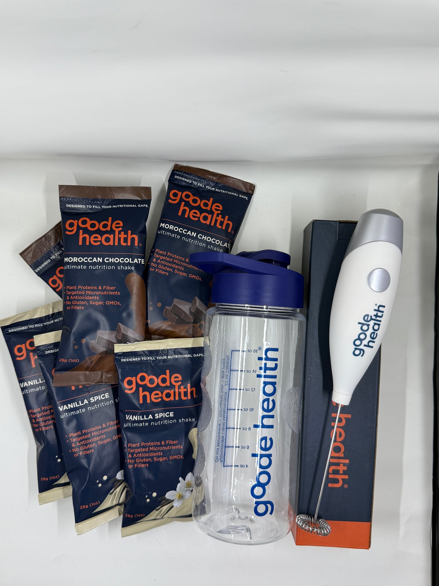 Good Health protein powder packets, mixer and shaker bottle on a white surface