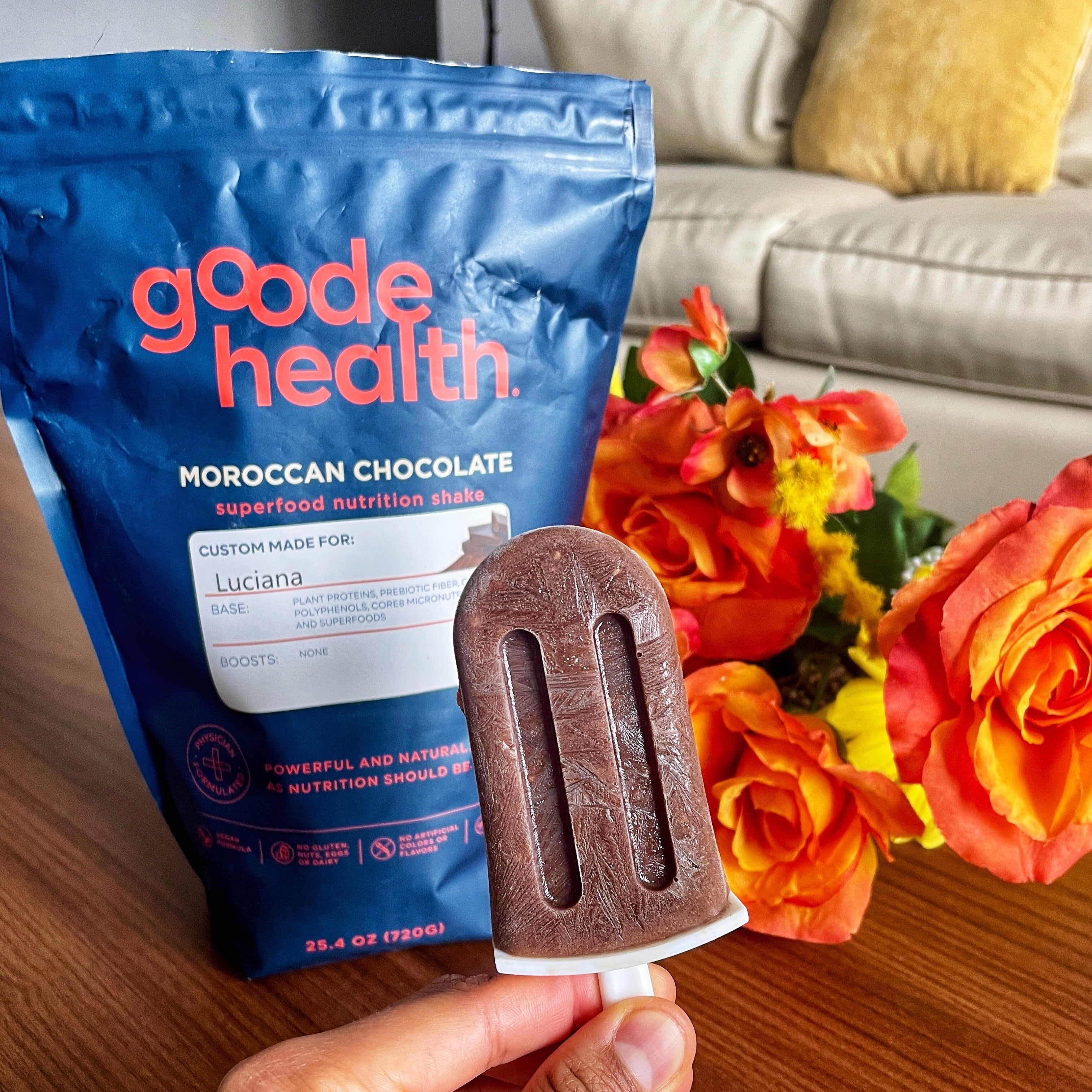 Chocolate popsicle held in front of a Goode Health package with flowers in the background or Moroccan Chocolate Coconut Popsicles