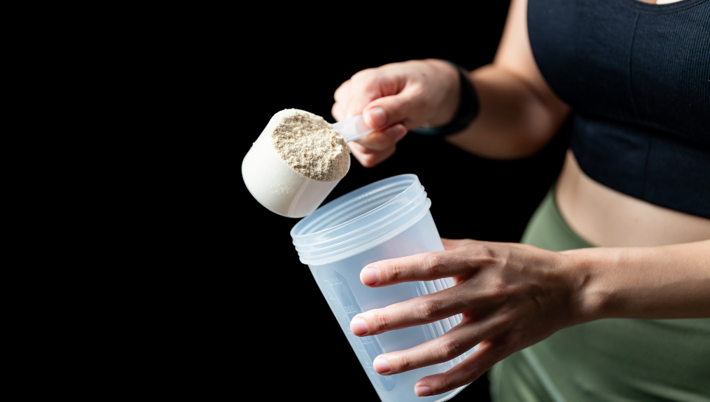 Fit woman in workout clothes putting a scoop of a super food supplement in an empty shake bottle