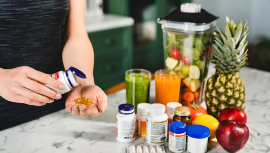 pills and fruit on a table has someone is pouring fish oil pills into their hand. Kitchen is green with white tops