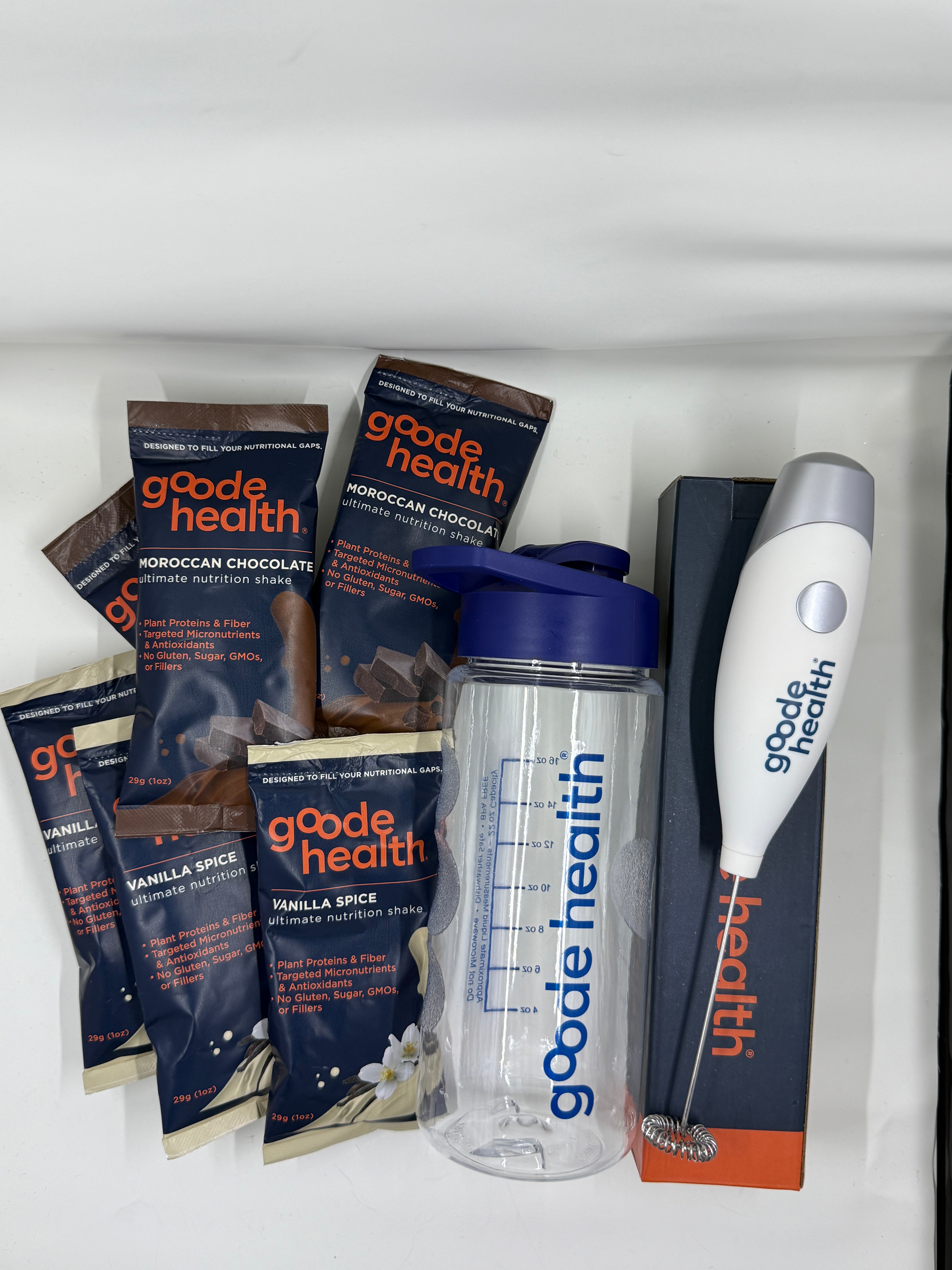 Good Health protein powder packets, mixer and shaker bottle on a white surface